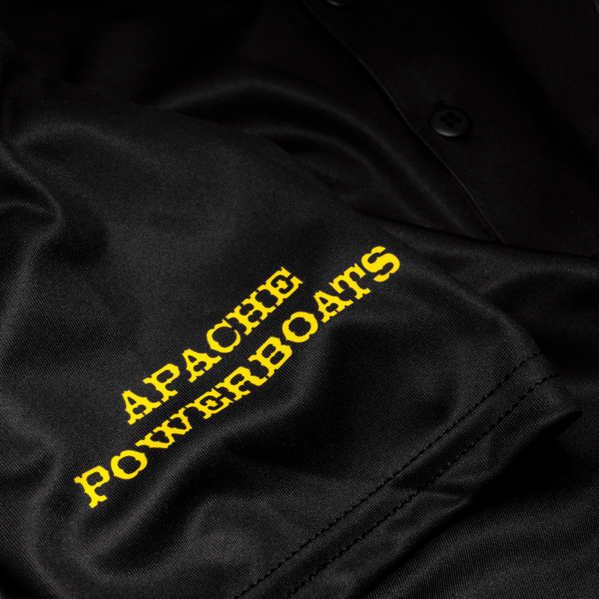 Close-up of Apache Powerboats sleeve logo on black performance polo shirt